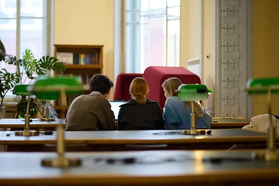 Drei Studierende sitzen von hinten an den Lesetischen einer Bibliothek