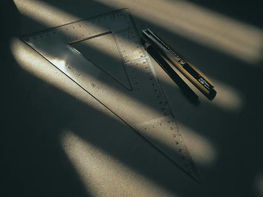 Zeichendreieck und Cuttermesser liegen im Sonnenlicht auf einem Tisch