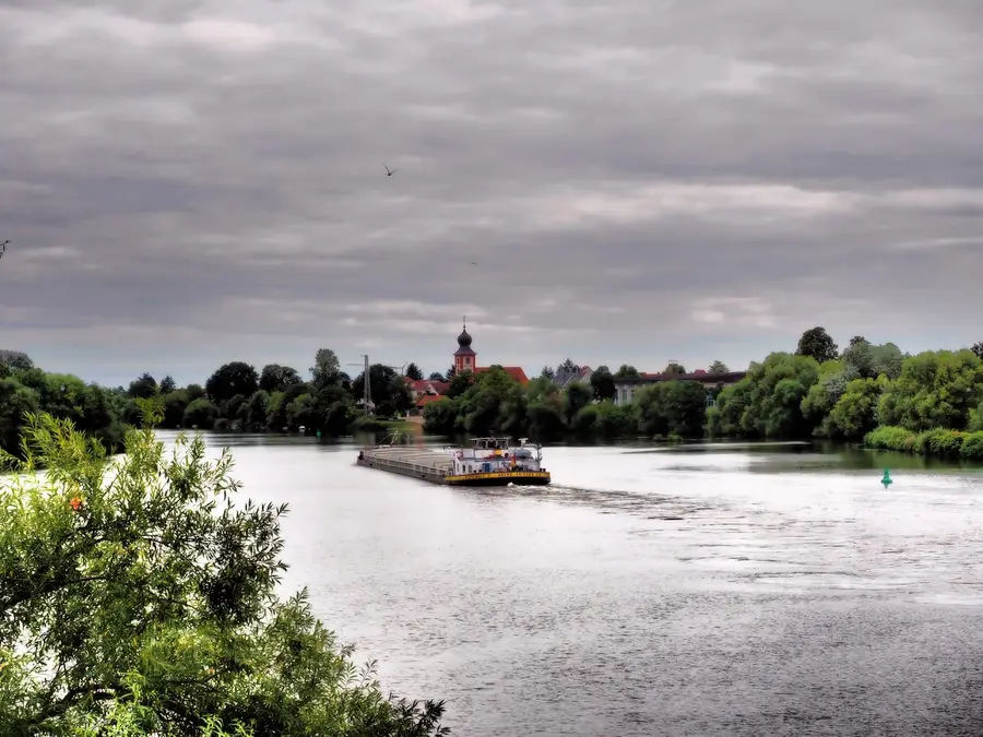 Beladenes Binnenschiff fährt auf einem Fluss an einem Ort vorbei