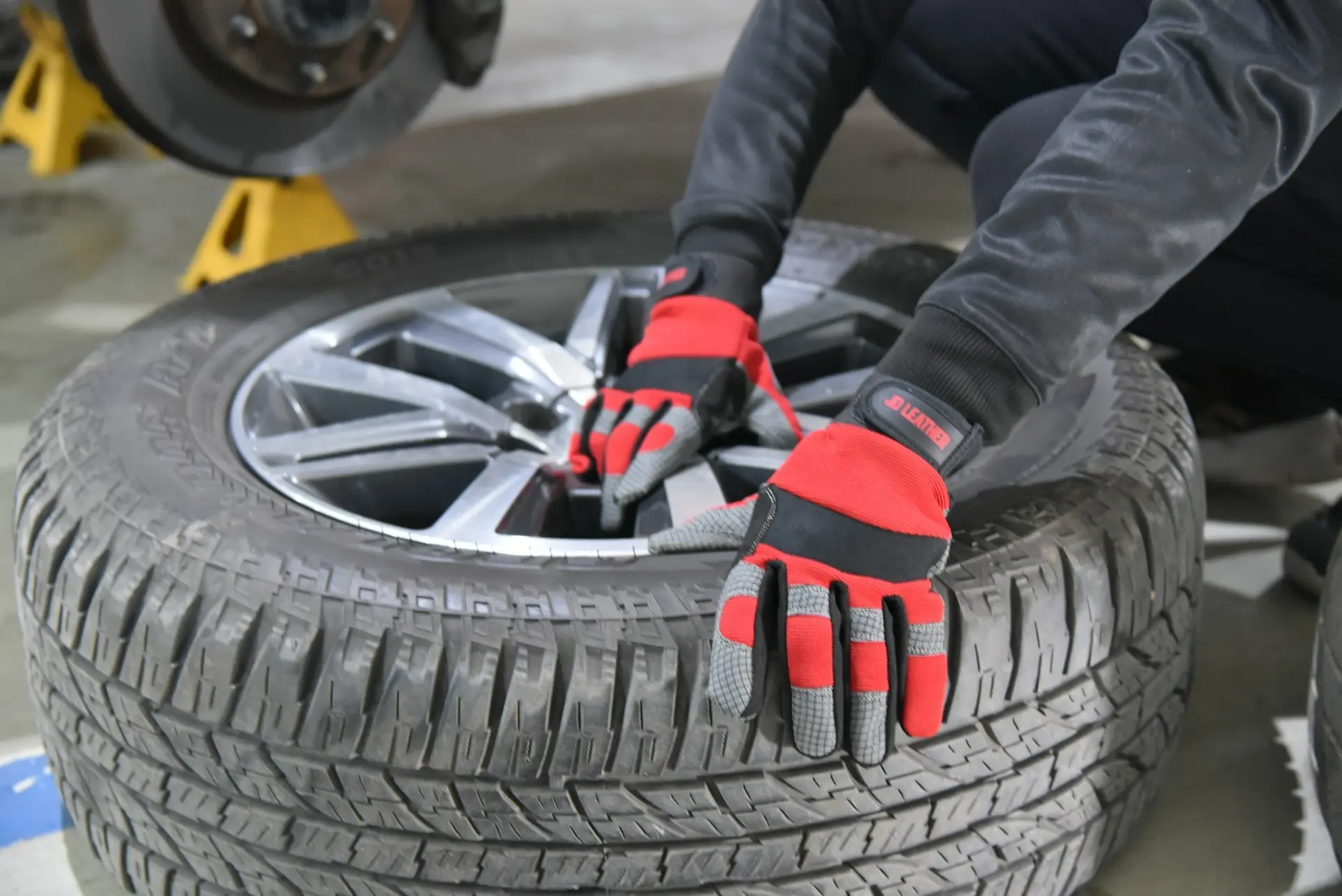 Hände mit Arbeitshandschuhen greifen einen Autoreifen in einer Werkstatt