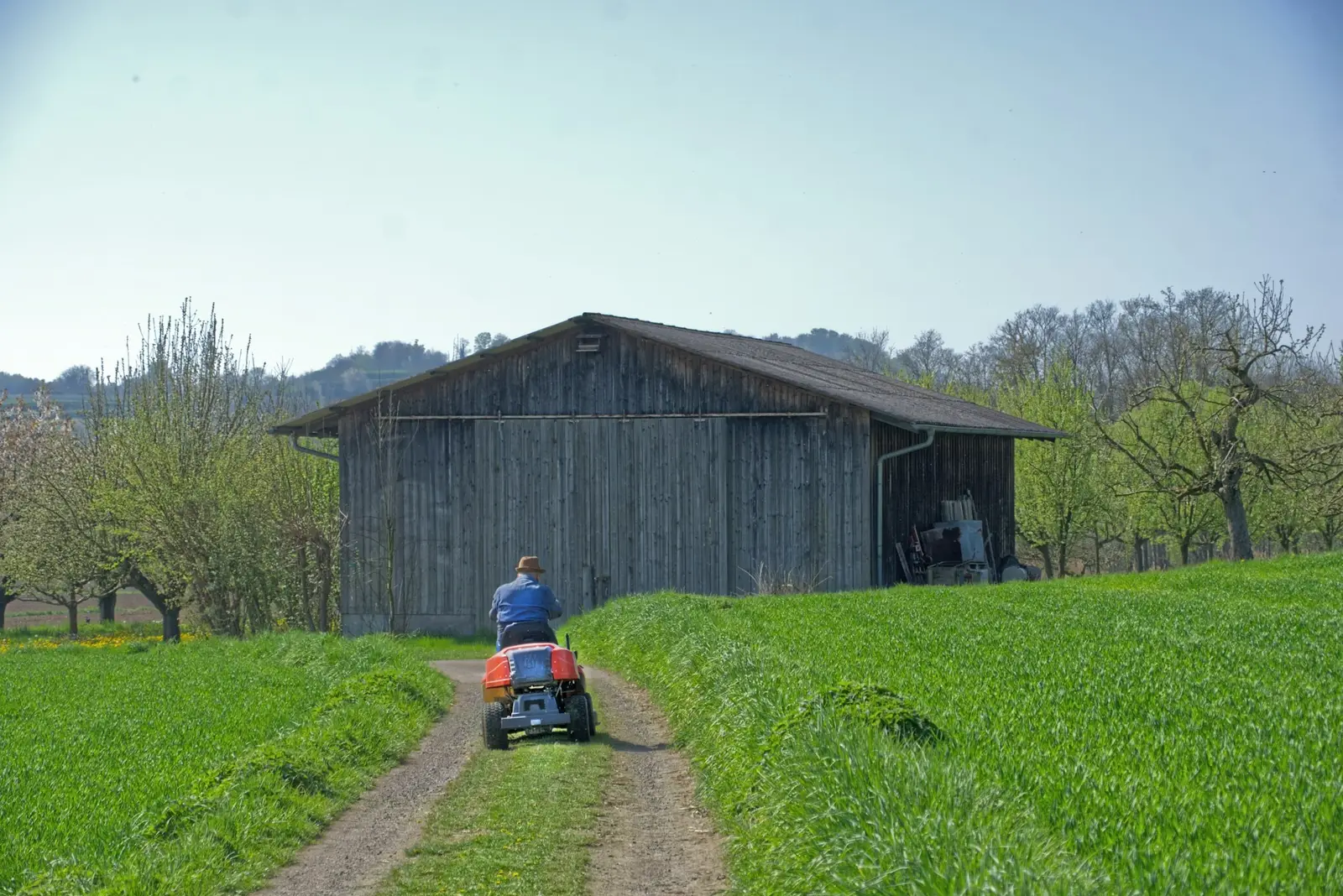 Eine Person fährt einen kleinen Traktor auf einem Weg zu einer hölzernen Scheune