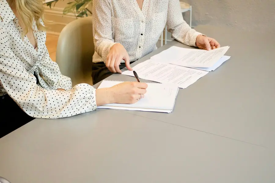 Zwei Personen sehen gemeinsam Unterlagen durch; eine hält einen Stift.