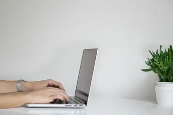 Hände arbeiten am Laptop an einem hellen Tisch