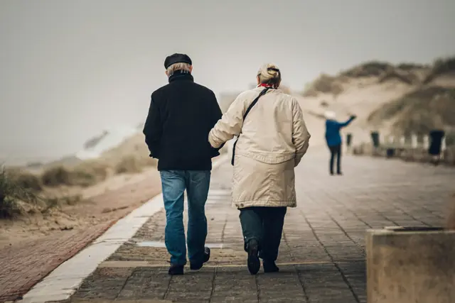 Ein älteres Paar geht Hand in Hand einen Weg durch die Dünen entlang