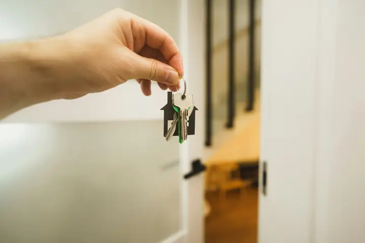 Eine Hand hält Wohnungsschlüssel vor einer geöffneten Tür.