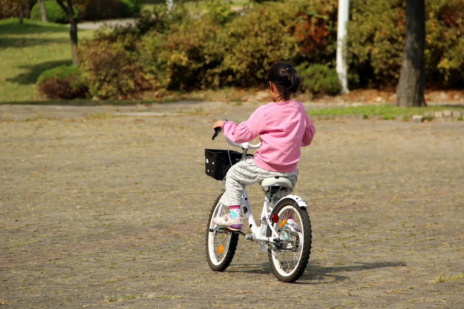Ein Kind im rosa Oberteil fährt auf einem Fahrrad über einen gepflasterten Platz