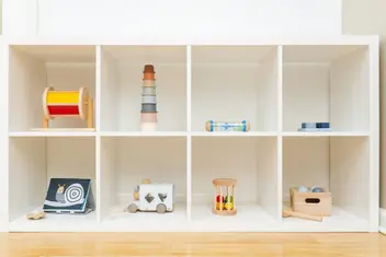 Niedriges weißes Regal mit Holzspielzeug in einem hellen Raum