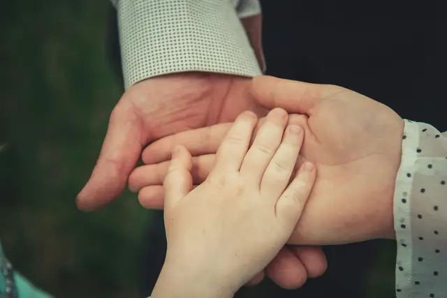 Eine Kinderhand liegt in den geöffneten Händen zweier Erwachsener
