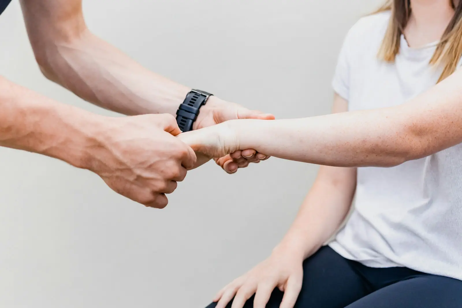 Eine behandelnde Person unterstützt das Handgelenk einer Patientin bei einer Übung