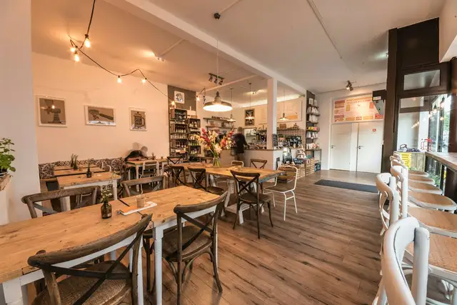 Kleines Ladencafé mit Holztischen, Regalen und Blumen auf dem Tresen