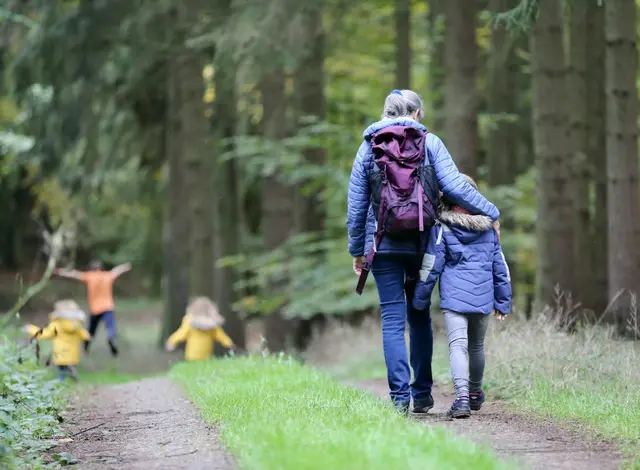 Familie geht einen Waldweg entlang, zwei Kinder in Regenjacken laufen voraus