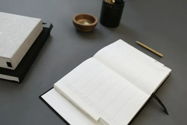 Aufgeschlagener Kalender mit leeren Wochenseiten, daneben ein Buch und ein Stift
