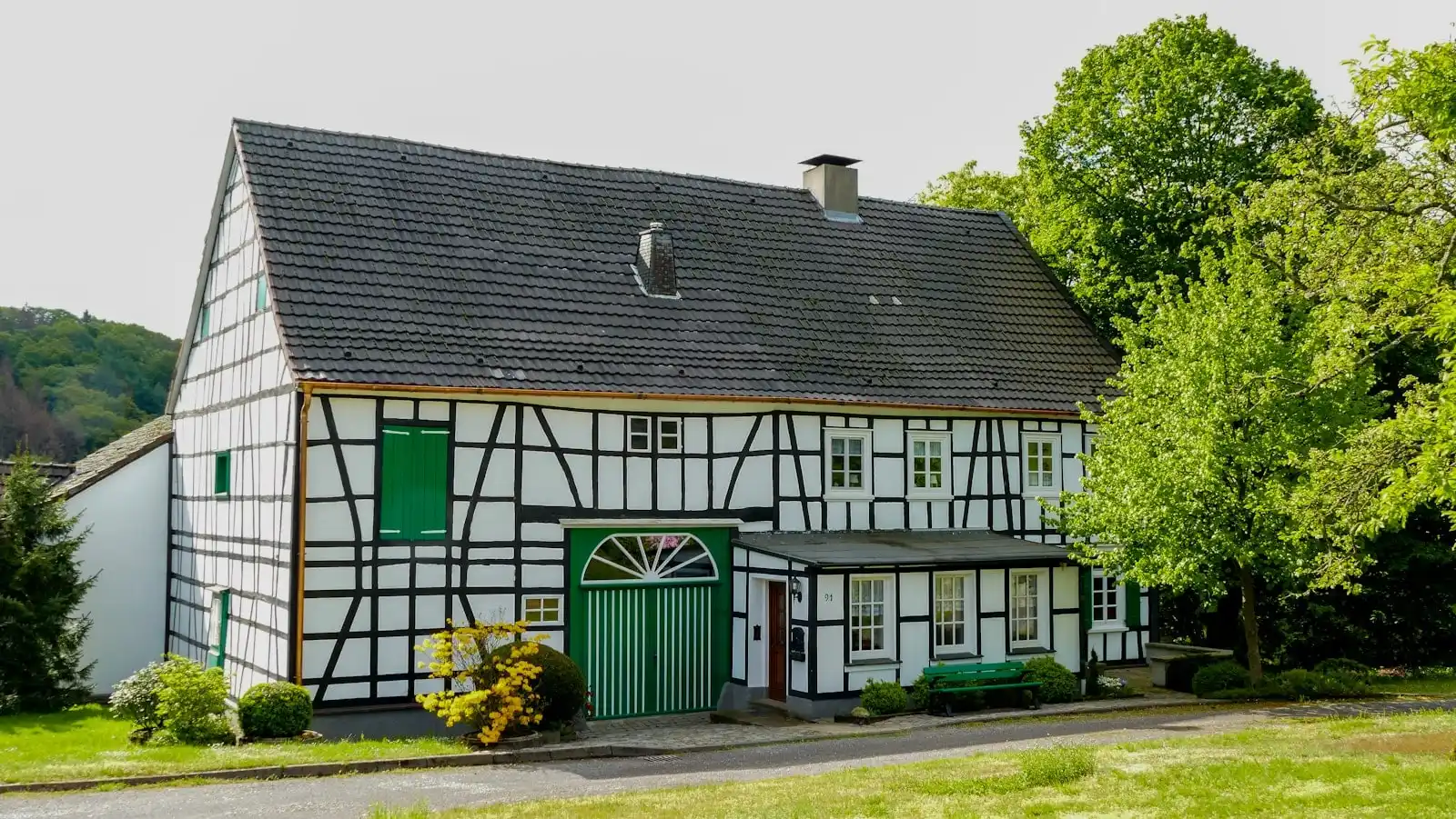 Fachwerkhof mit dunklem Dach und grünen Toren, davor Rasen und Bäume