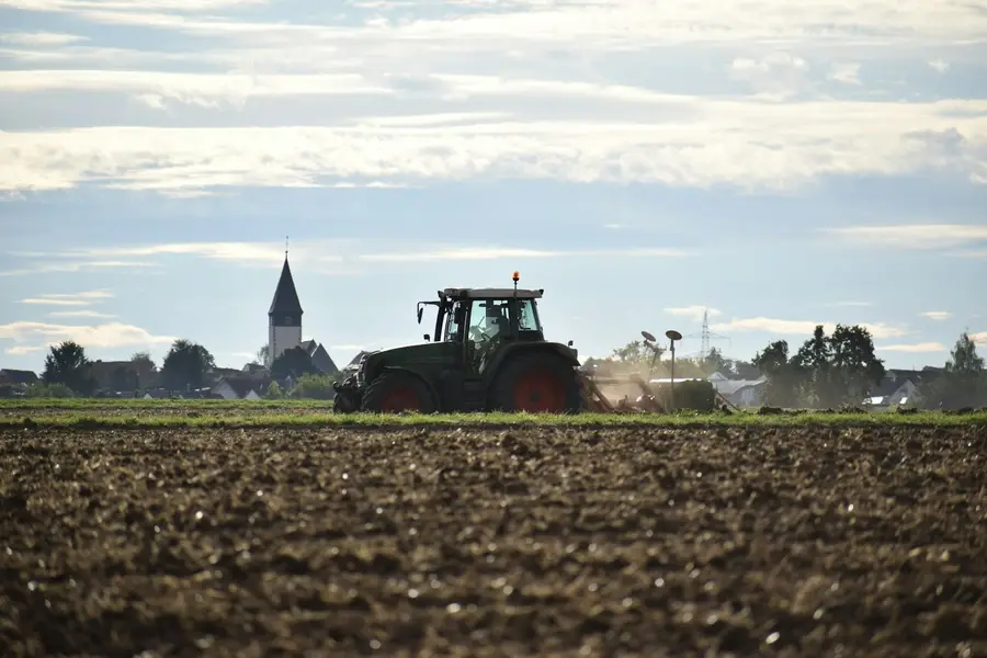 Traktor pflügt einen Acker, dahinter ein Dorf mit Kirchturm