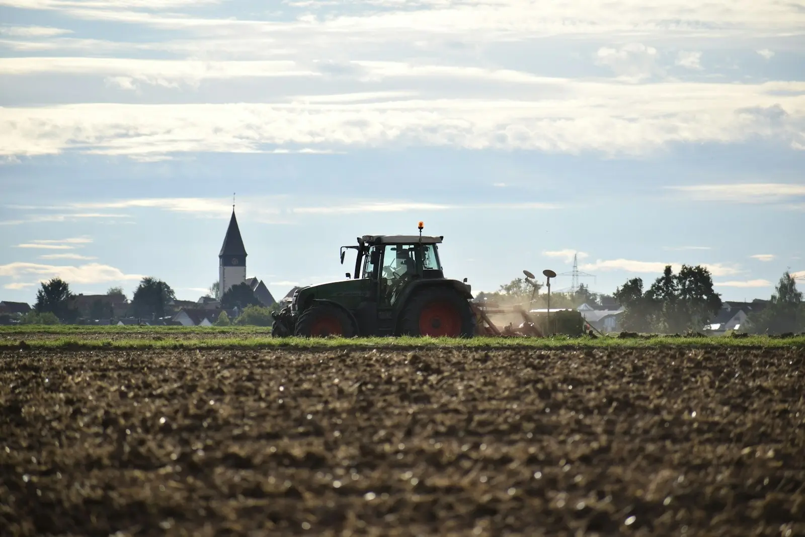 Traktor pflügt einen Acker, dahinter ein Dorf mit Kirchturm