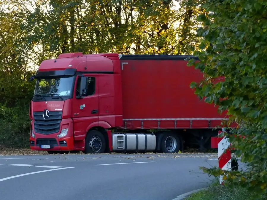 Roter Sattelzug mit Planenaufbau steht an einer Landstraße am Waldrand
