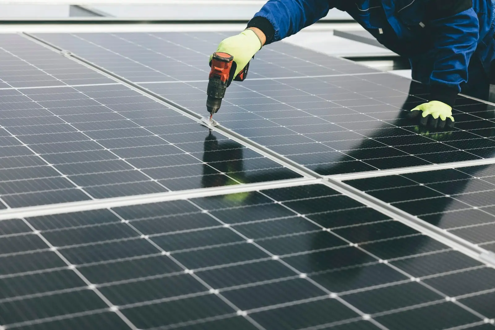 Person mit Arbeitshandschuhen befestigt Solarmodule mit einem Akkuschrauber