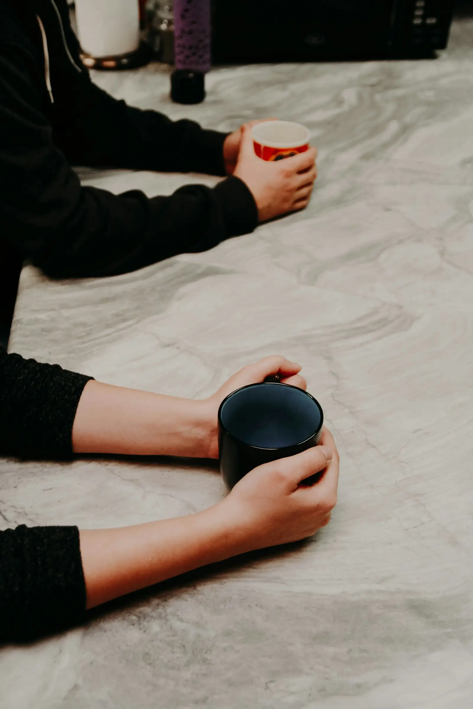Zwei Menschen sitzen sich an einem hellen Steintisch gegenüber, jeder hält eine Tasse