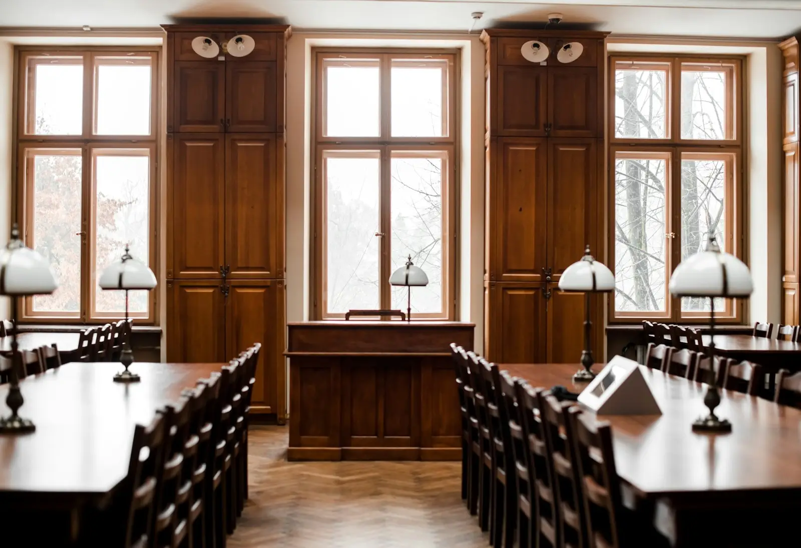 Holzvertäfelter Saal mit langen Tischen und Bankierslampen