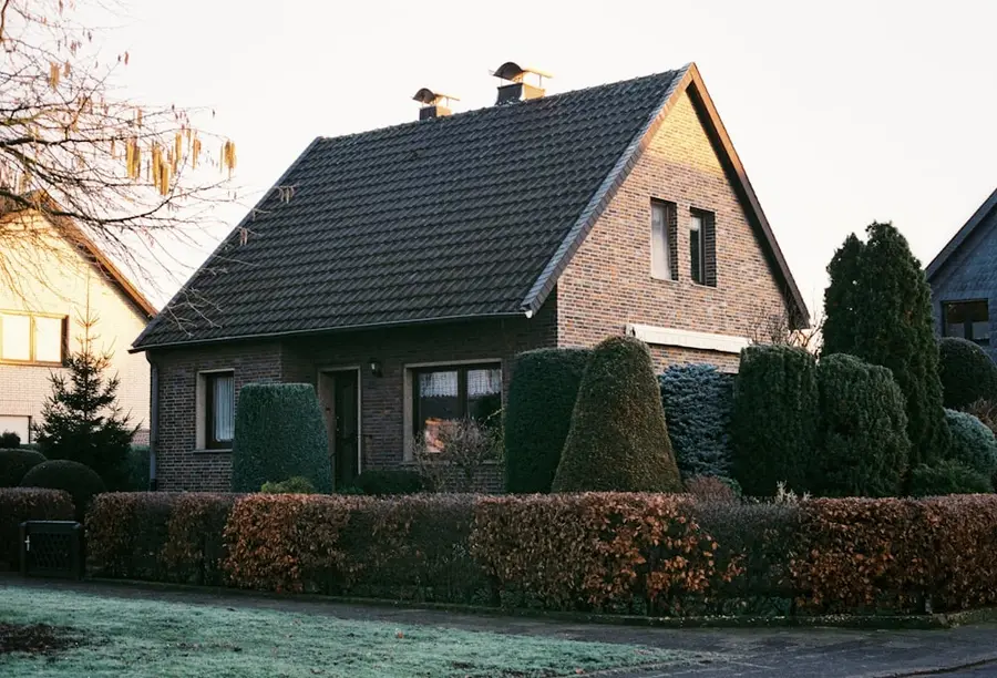 Einfamilienhaus mit Satteldach hinter einer geschnittenen Hecke